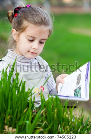 Portrait of cute schoolgirl reading interesting book in natural environment