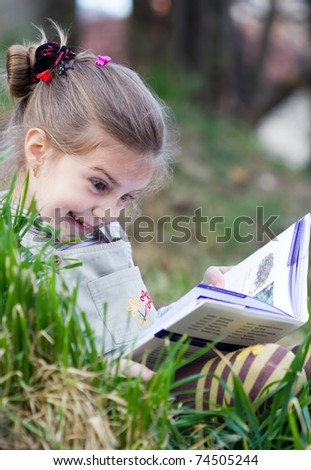 Portrait of cute schoolgirl reading interesting book in natural environment