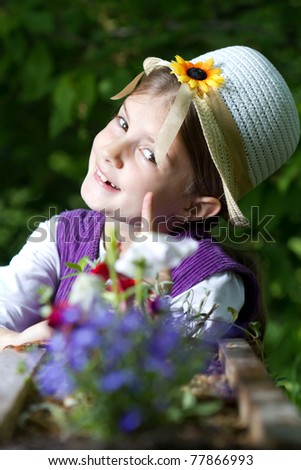 Little beautiful girl in hat posing and smiling behind the flowers