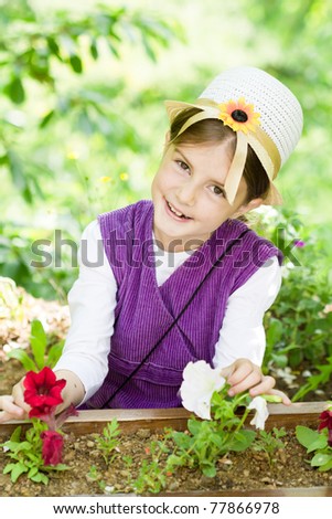 Little beautiful girl in hat posing and smiling behind the flowers