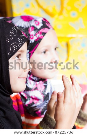 Two little muslim girls praying with hands up