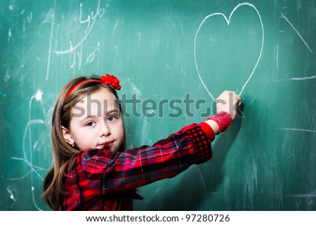 Pretty little girl drawing heart on blackboard