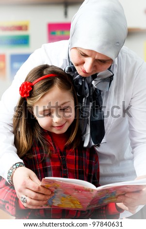 little schoolgirl with her young teacher in the classroom
