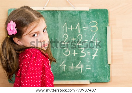 Confused schoolgirl standing in front of blackboard - problem with mathematics