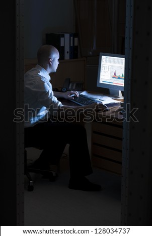 Late night office worker working overtime. White collar worker working on computer at night in dark office.