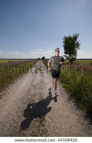 Athletic male running on a field road on a hot summer day.