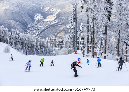 Skiers and snowboarders riding on a ski slope in Sochi mountain resort on snowy winter background