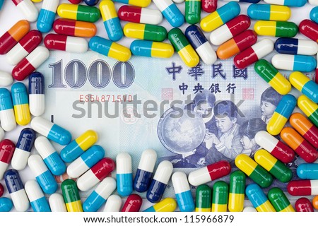 An overhead shot of a one thousand NT dollar bill covered with colorful pills on a white background.