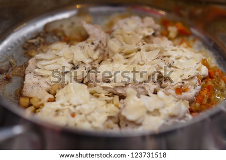 White meat breast cooking in stainless steel pan with vegetables and almond flakes on gas stove (italian recipe)