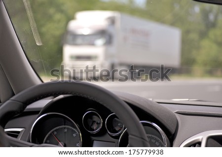 Steering wheel of a car while driving with truck in background