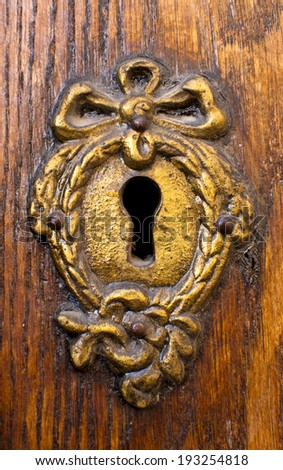 Close-up shot of an antique keyhole in a rusted iron plate on a wooden door