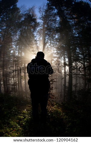 silhouette of man standing in sunbeams in forest