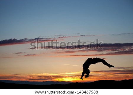 silhouette of gymnast doing back handspring in sunset