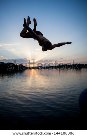 silhouette of man jumping in lake in sunset