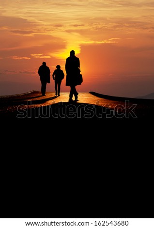 silhouetted people walk over bridge in sunset