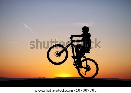 silhouette of boy riding his mountain-bike in sunset