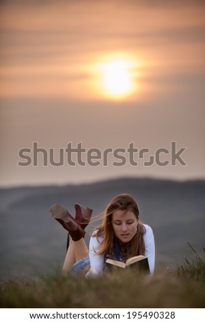 young woman lies in grass and reads book in sunset