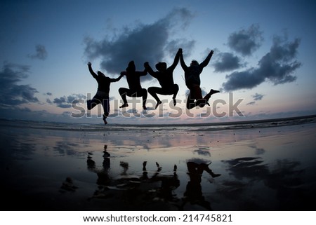 silhouetted friends jumping in sunset at beach