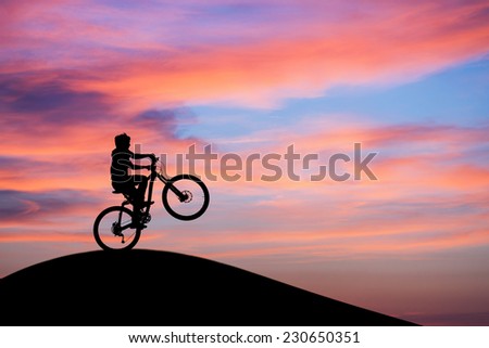 silhouetted mountainbiker doing wheelie in sunset sky on hill