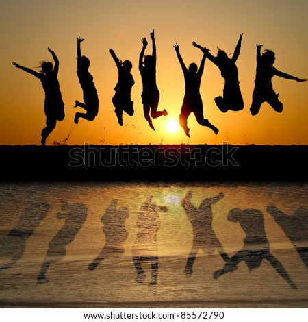 silhouette of friends jumping in sunset at beach with reflection in water