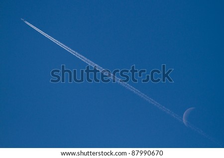 jet stream of airplane going through the moon in blue sky