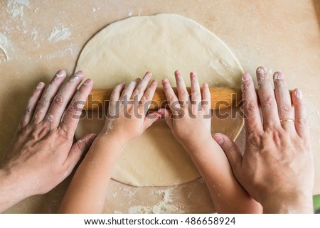 Children and dad hands rolled dough with a rolling pin on the table