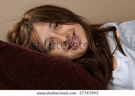 Young pretty brunette hispanic teenage girl with messy hair smiling laying on pillow with braces