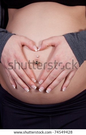 Close up of a womans hands in shape of heart over pregnant belly button