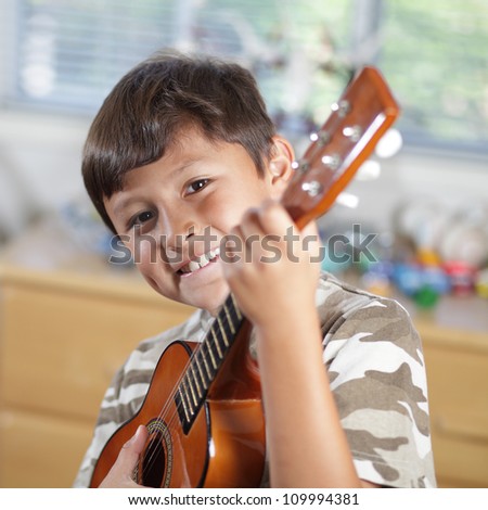 A young smiling boy plays his guitar or ukulele