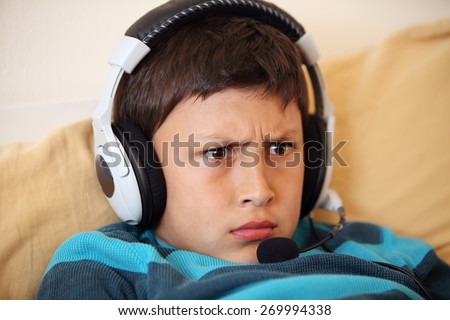 Close-up of young boy frowning while playing video game with his friends with headset and microphone