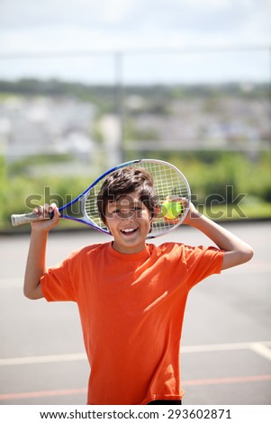 Young boy outside in sun with tennis racquet and ball - portrait format with copy space above