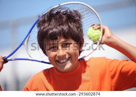 Young boy outside in sun with tennis racquet and ball - landscape format with copy space above