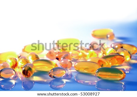 Various yellow and orange pills and capsules on a blue and white background with saturated colors and copy space