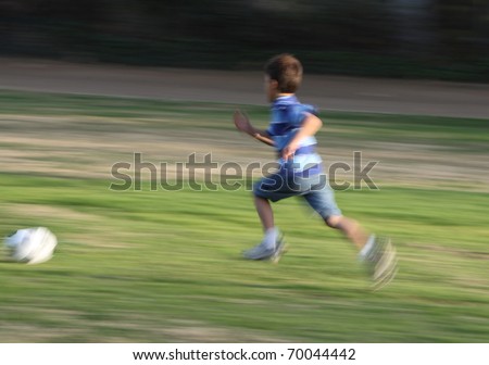 Motion blurred boy running fast after soccer ball on green grassy background