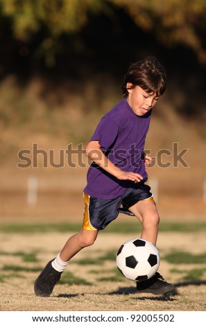 Boy in purple shirt plays soccer in the late afternoon sunlight