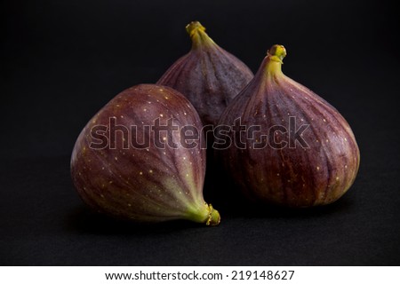 A closeup of three figs on the dark background
