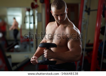 Muscular man working out with dumbbells looking to his biceps black and white