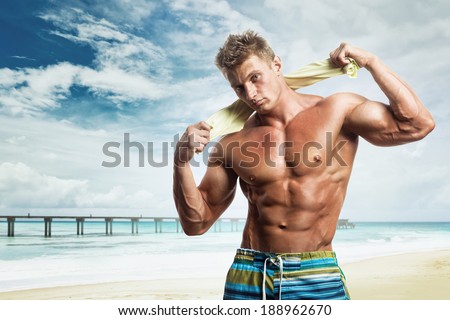 Handsome young muscular male model on the beach enjoying summer