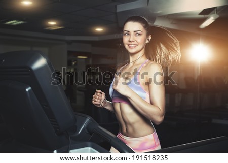 Young sporty woman running on machine in the gym and listening music in headphones