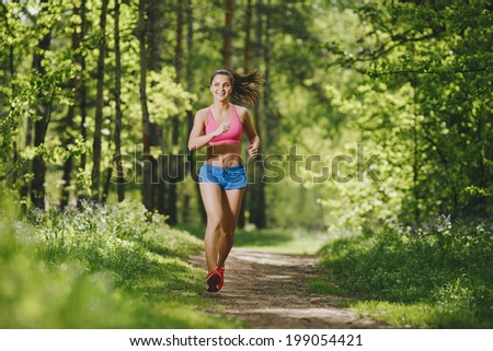 fitness girl running on forest trail and smiling. beautiful woman runs in park
