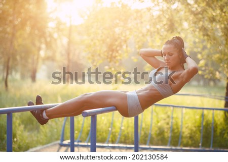 beautiful fitness woman doing exercise on bars sunny outdoor. Sporty girl doing sit-ups on bars outdoors