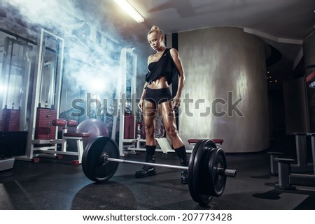 fitness blonde girl prepares for exercising with barbell in gym