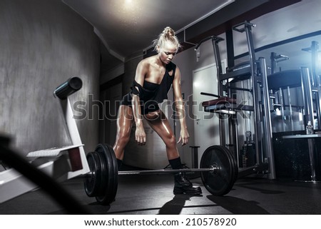 fitness blonde girl prepares for exercising with barbell in gym