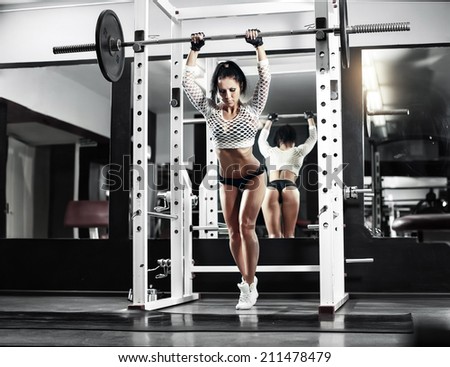 Young sexy girl in the gym doing squat with barbell