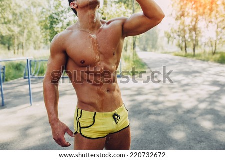 Young exhausted athlete splashing and pouring fresh water on his head to refresh during a running trail
