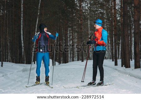 Two skiers cross-country ski  talk in winter forest