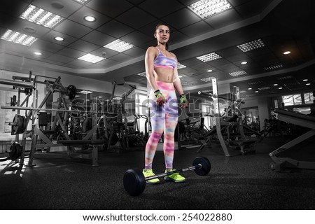 The fitness girl prepares for exercising with barbell in gym