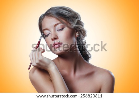 Closeup portrait of a woman applying dry cosmetic tonal foundation on the face using makeup brush.