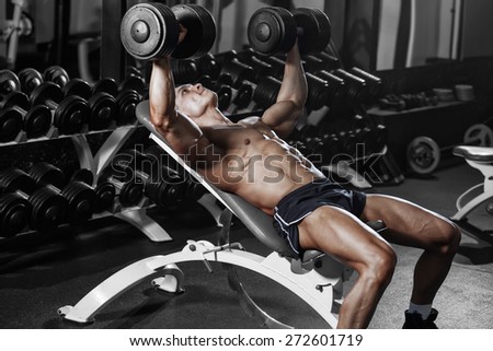 Athlete muscular bodybuilder training chest an bench with dumbbell in the gym
