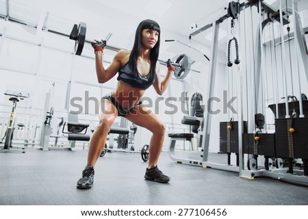 Young sexy girl in the gym doing squat with barbell